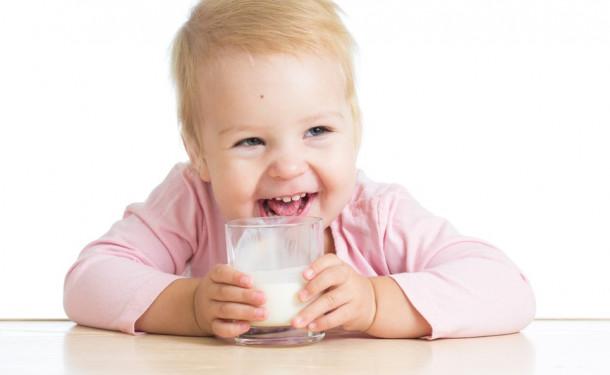 Ребенок сидит и пьет из чашки молоко
